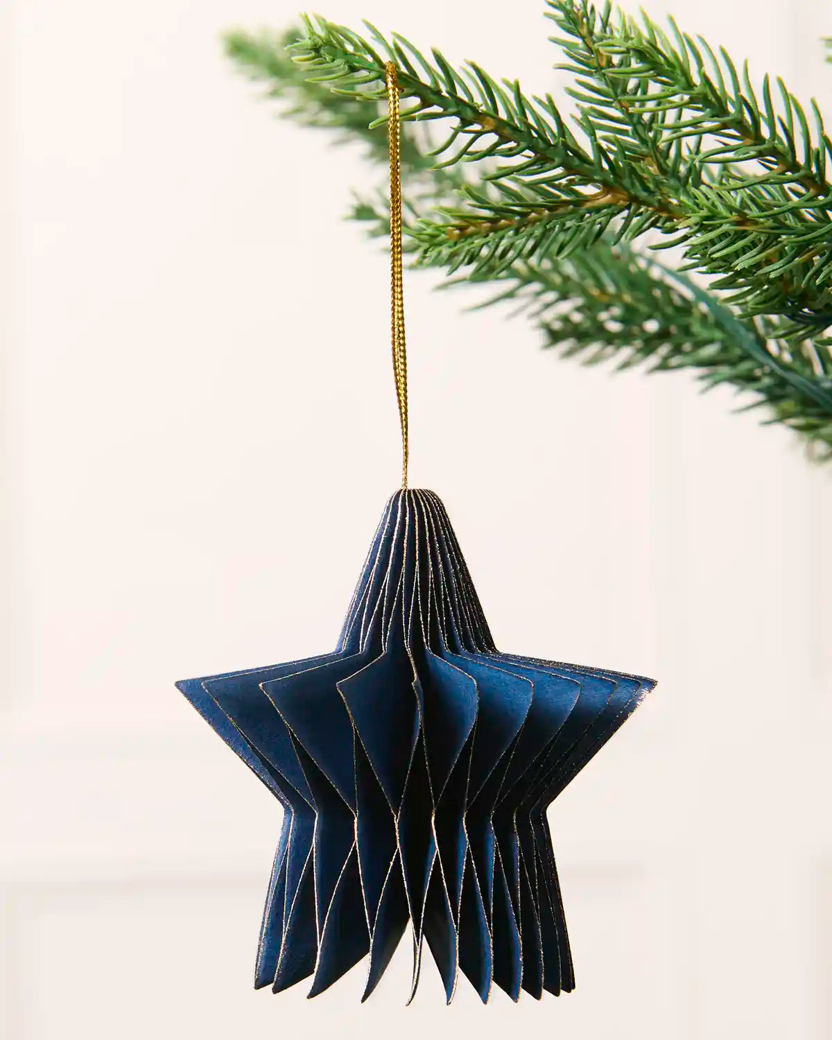 Close-up of a navy folded paper star decoration hanging from a Christmas tree.