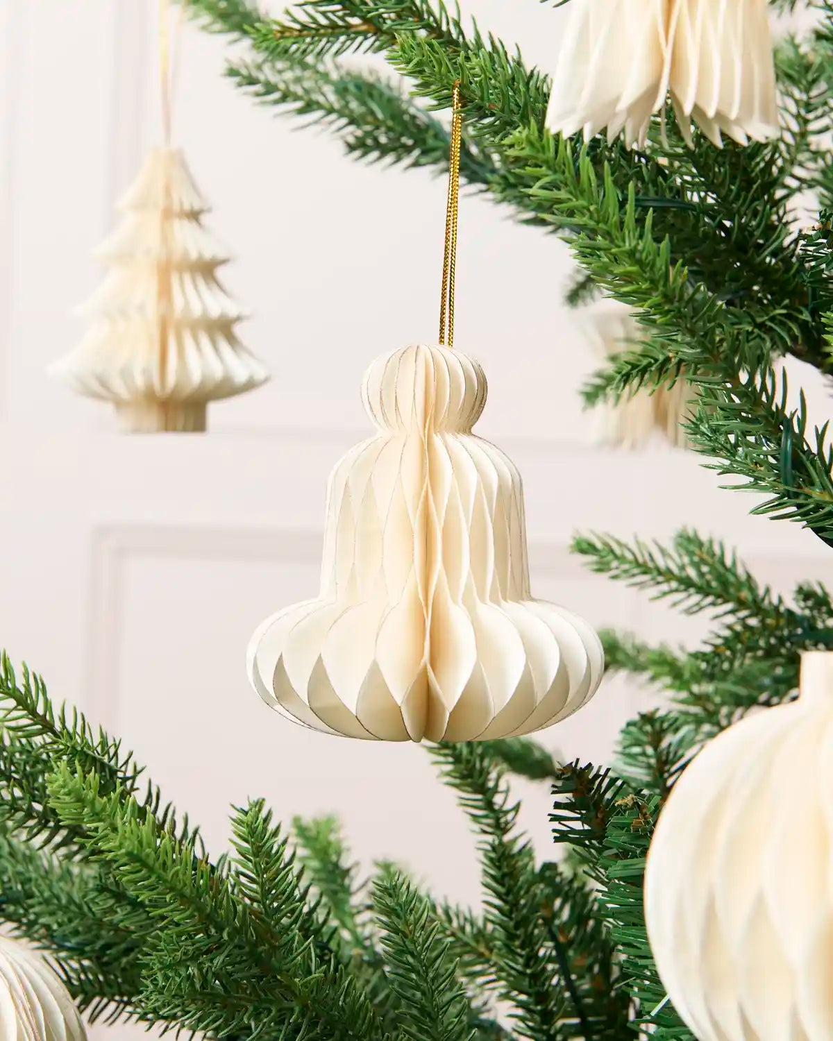 Close-up of an off-white folded paper bell decoration hanging from a Christmas tree.