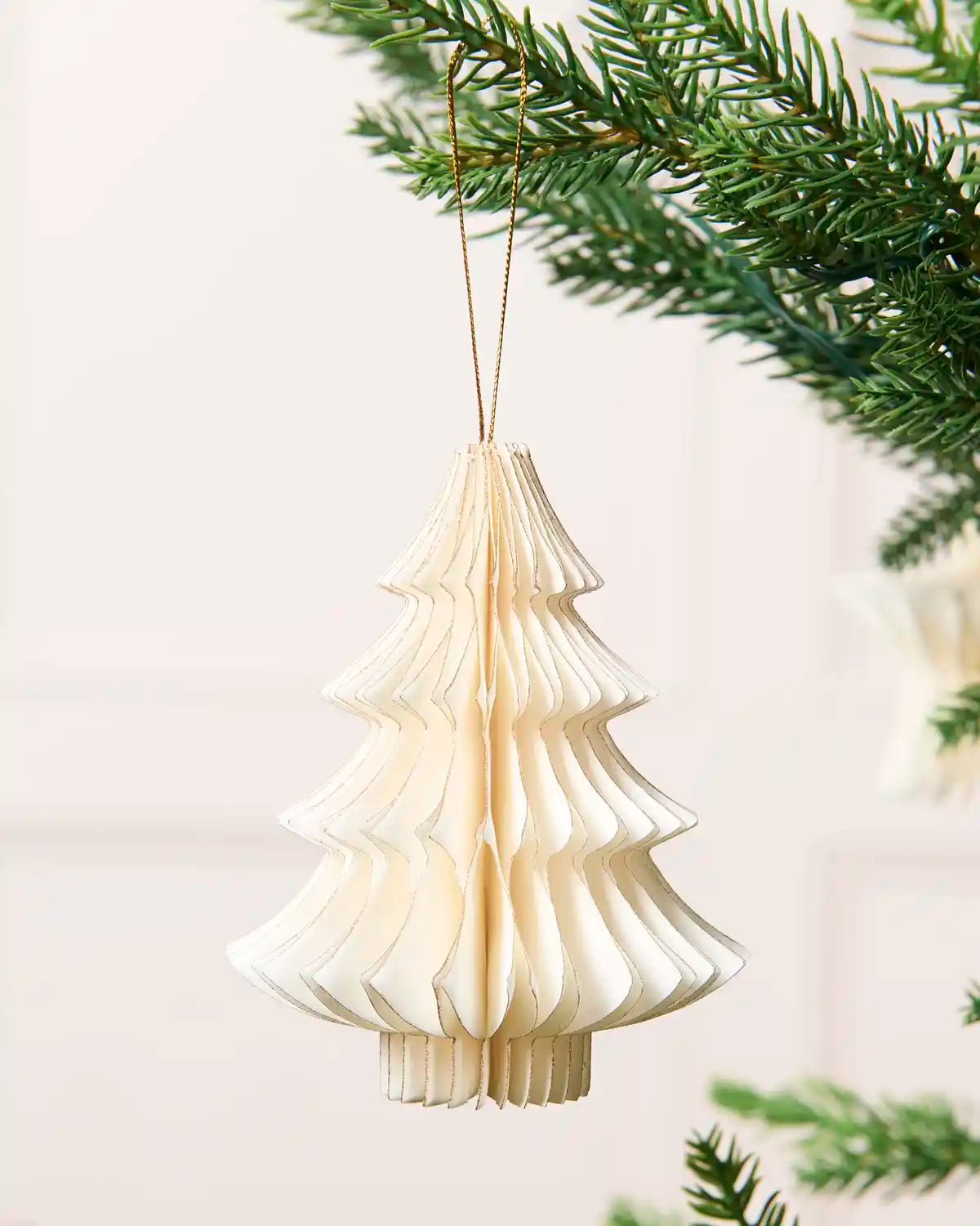 Close-up of an off-white folded paper Christmas tree decoration with gold glitter edging.