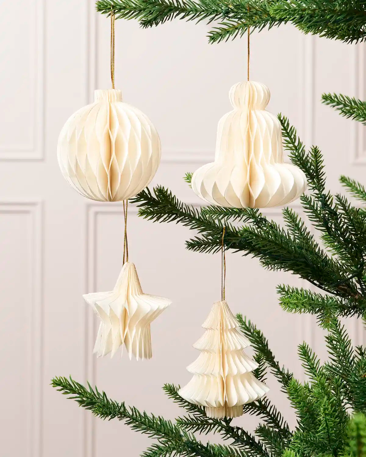 Off-white paper bauble, bell, star and Christmas tree decorations displayed on a Christmas tree.