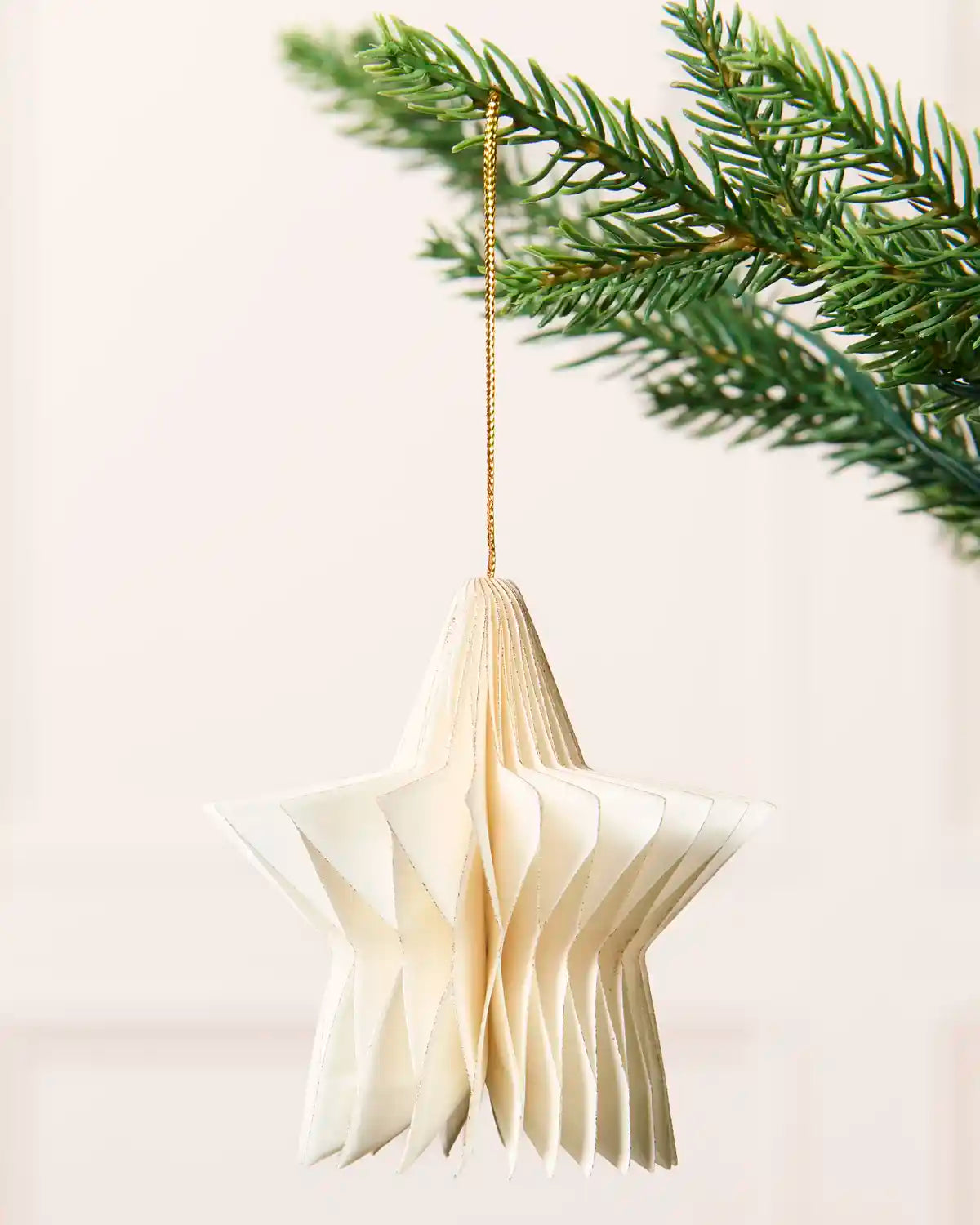 Close-up of an off-white folded paper star decoration hanging from a Christmas tree.