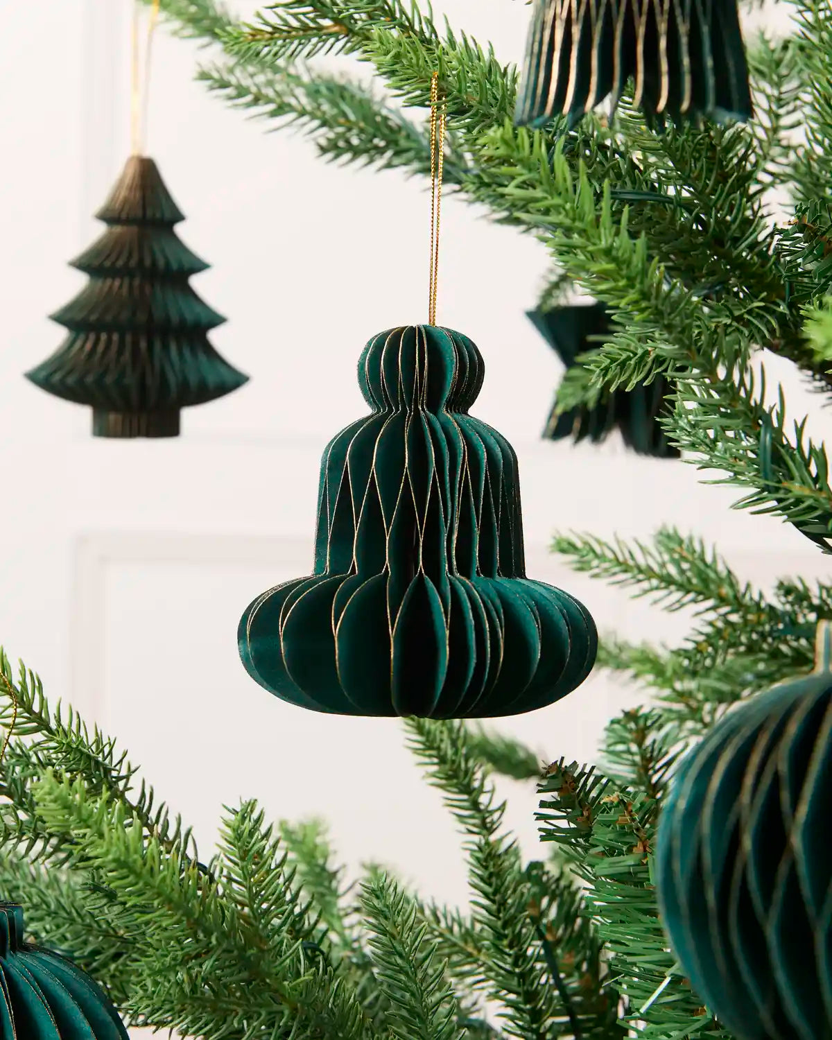 Close-up of a sage green folded paper bell decoration hanging from a Christmas tree.