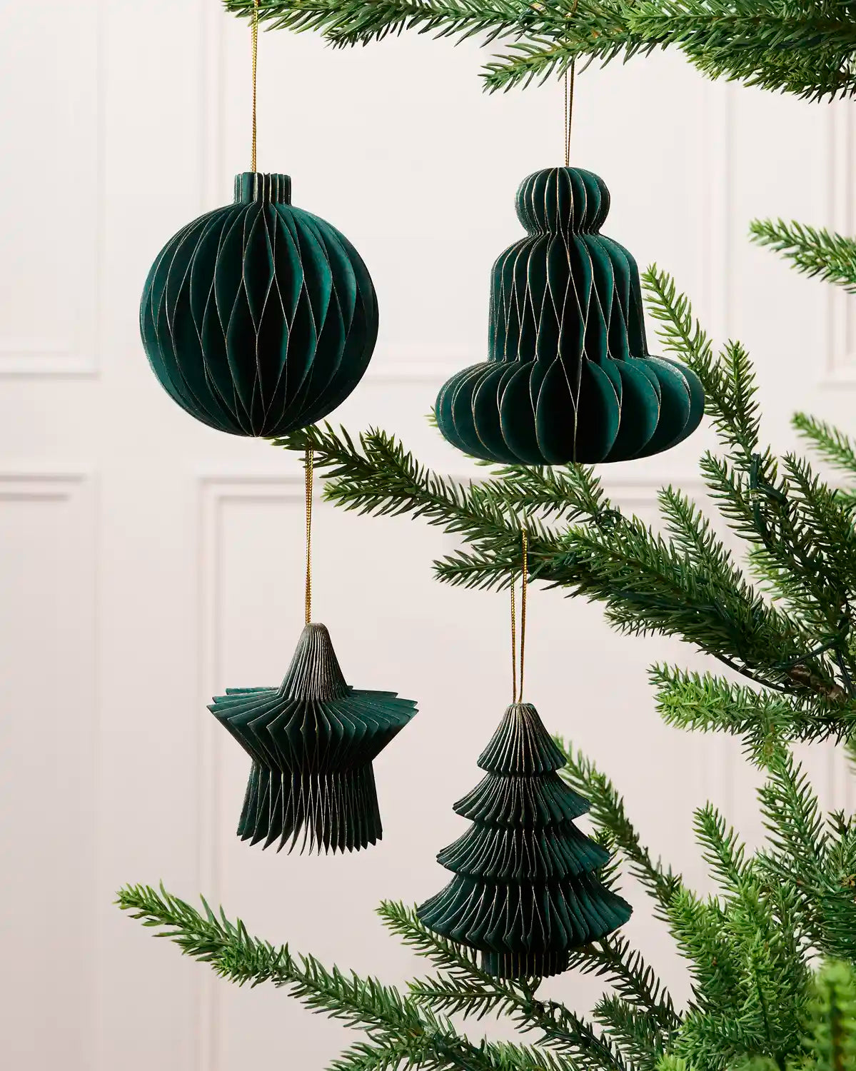 Sage green paper bauble, bell, star and Christmas tree decorations displayed on a Christmas tree.