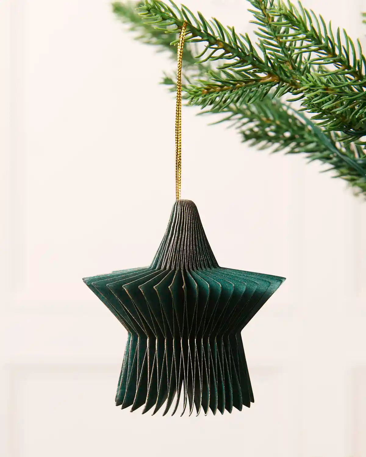 Close-up of a sage green folded paper star decoration hanging from a Christmas tree.