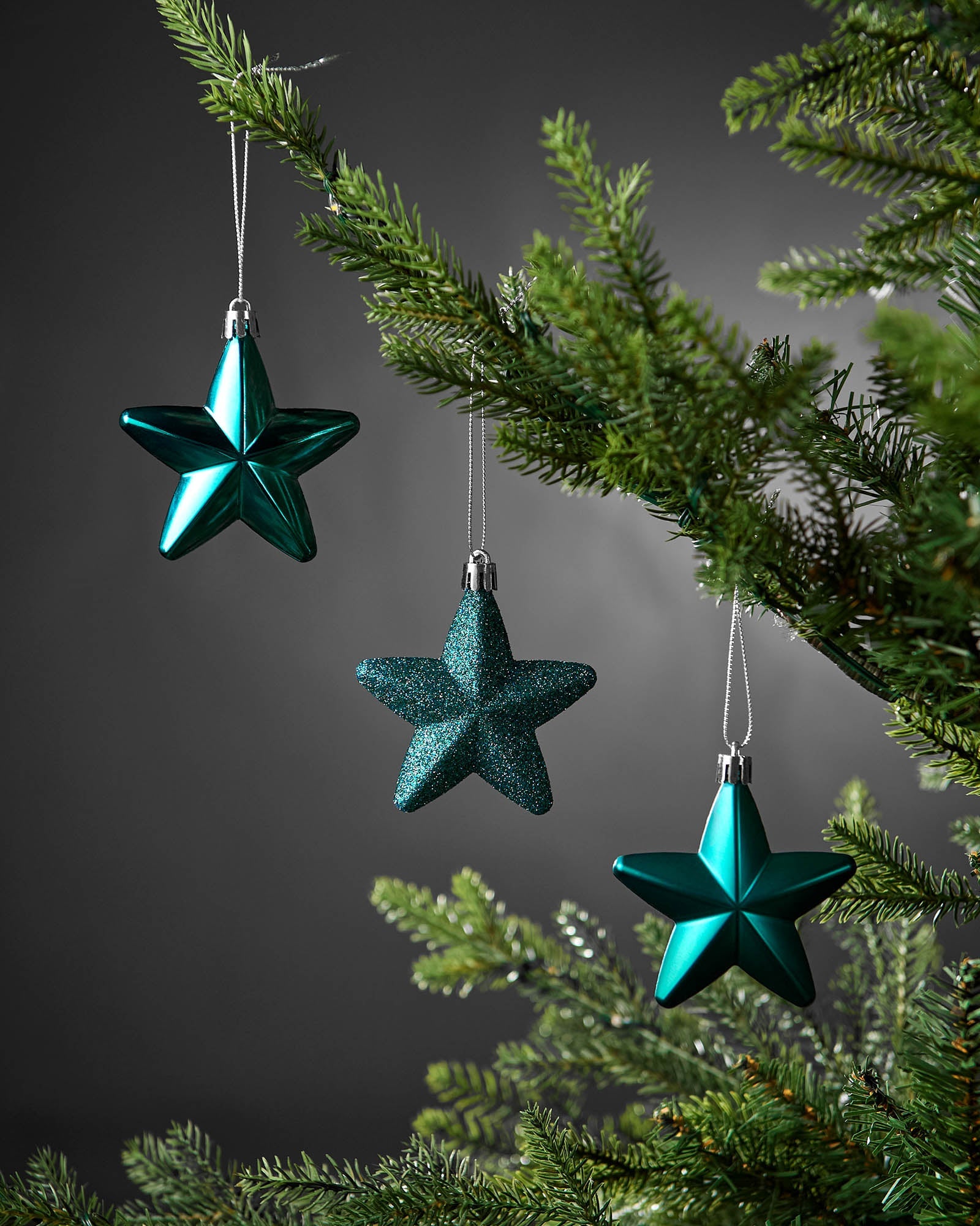 Set of 12 teal star decorations hanging from a Christmas tree, with shiny, Matte and glitter finishes.
