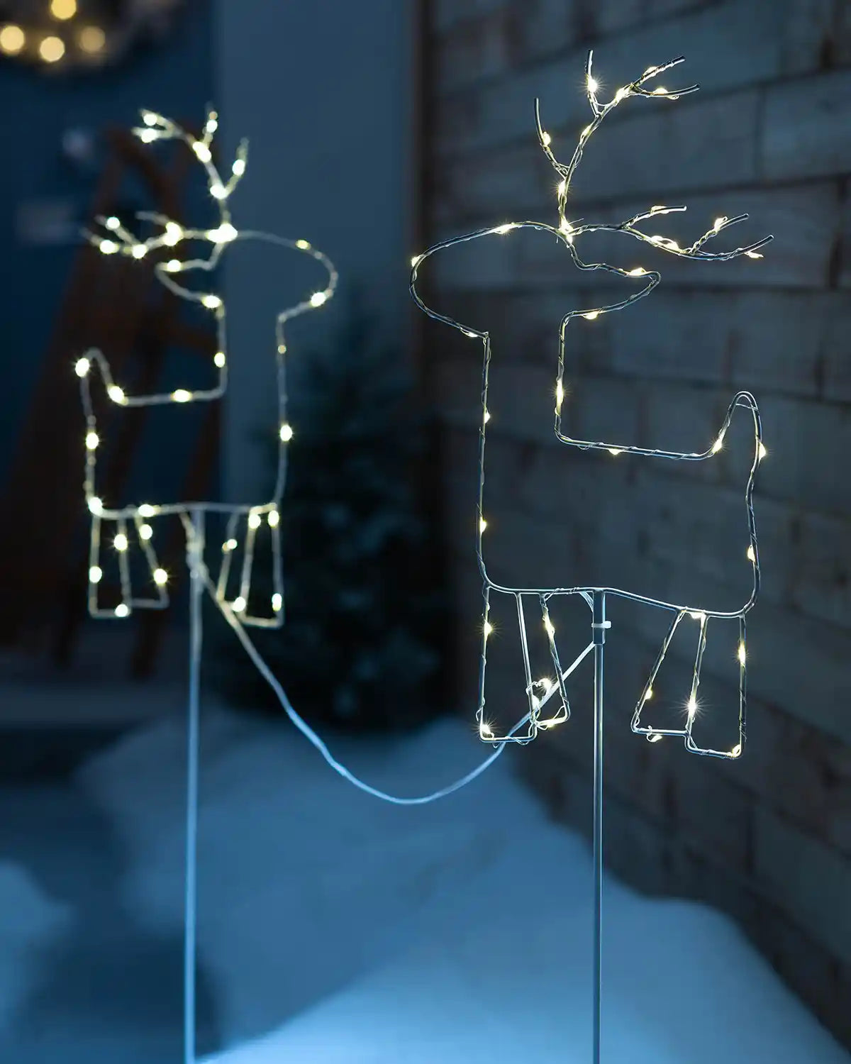 Pair of warm white LED reindeer pathway stake lights displayed outdoors in snow