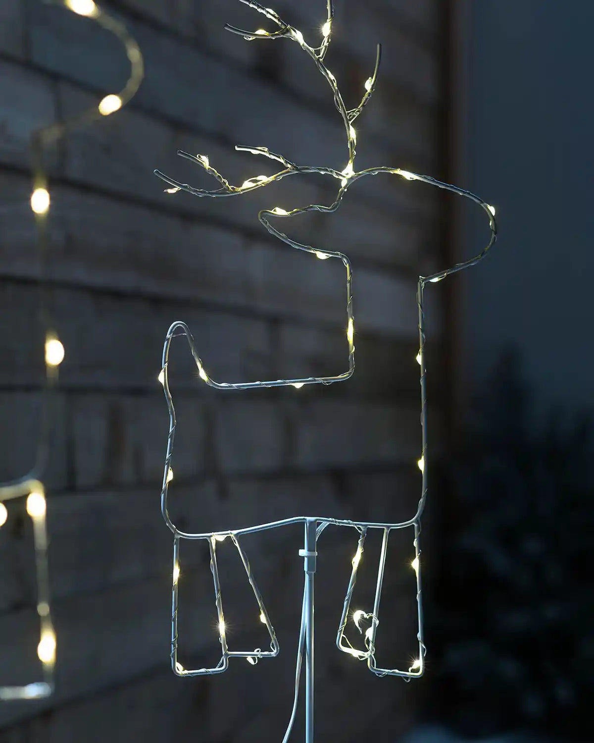Illuminated warm white LED reindeer pathway stake light outdoors at night