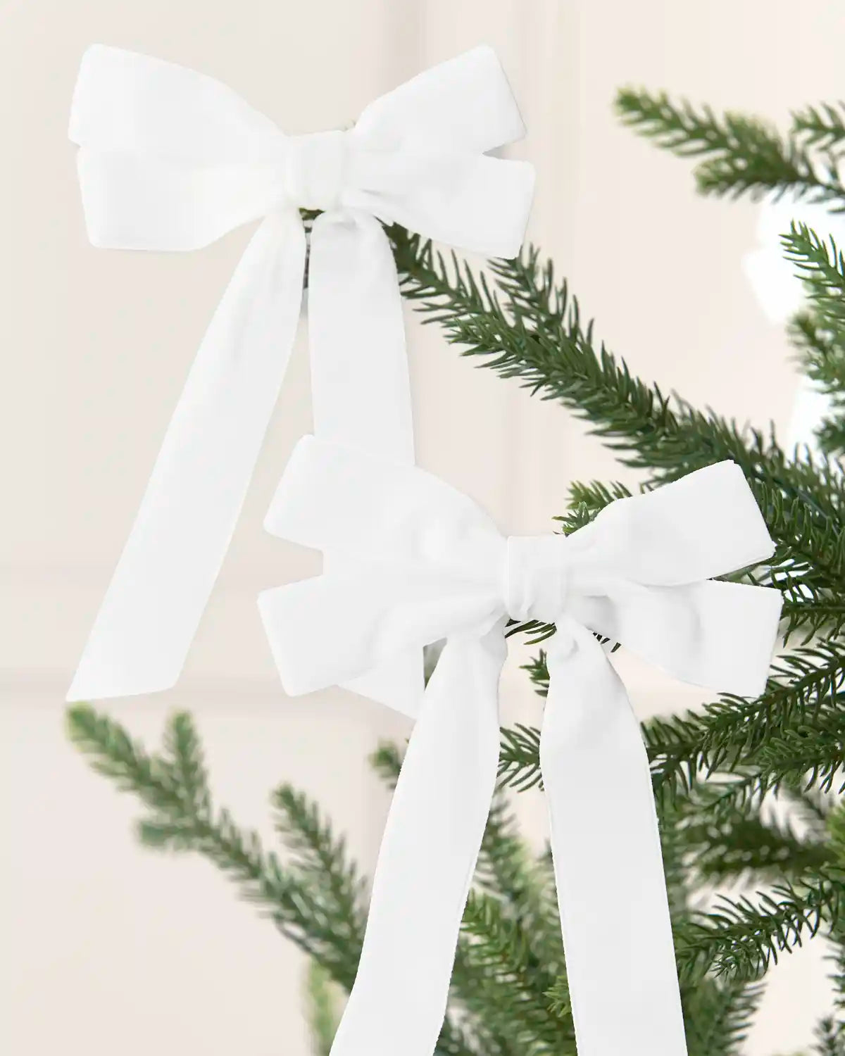 Two white velvet double bows with long tails arranged across Christmas tree branches.