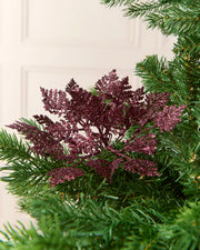 Burgundy 19 cm glitter leaf picks arranged among the branches of a Christmas tree.