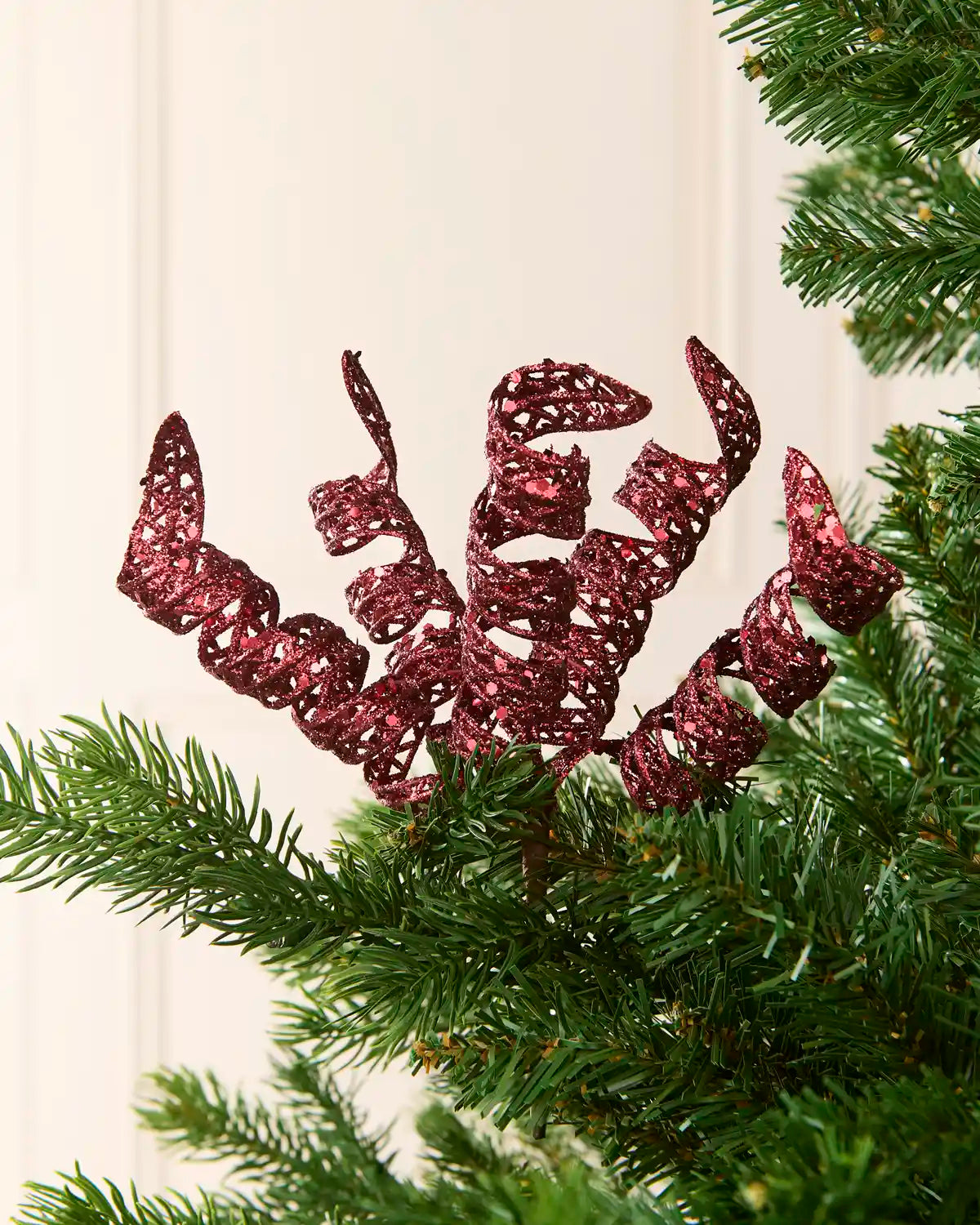 Set of three 18 cm burgundy glitter spiral picks arranged among green Christmas tree branches.
