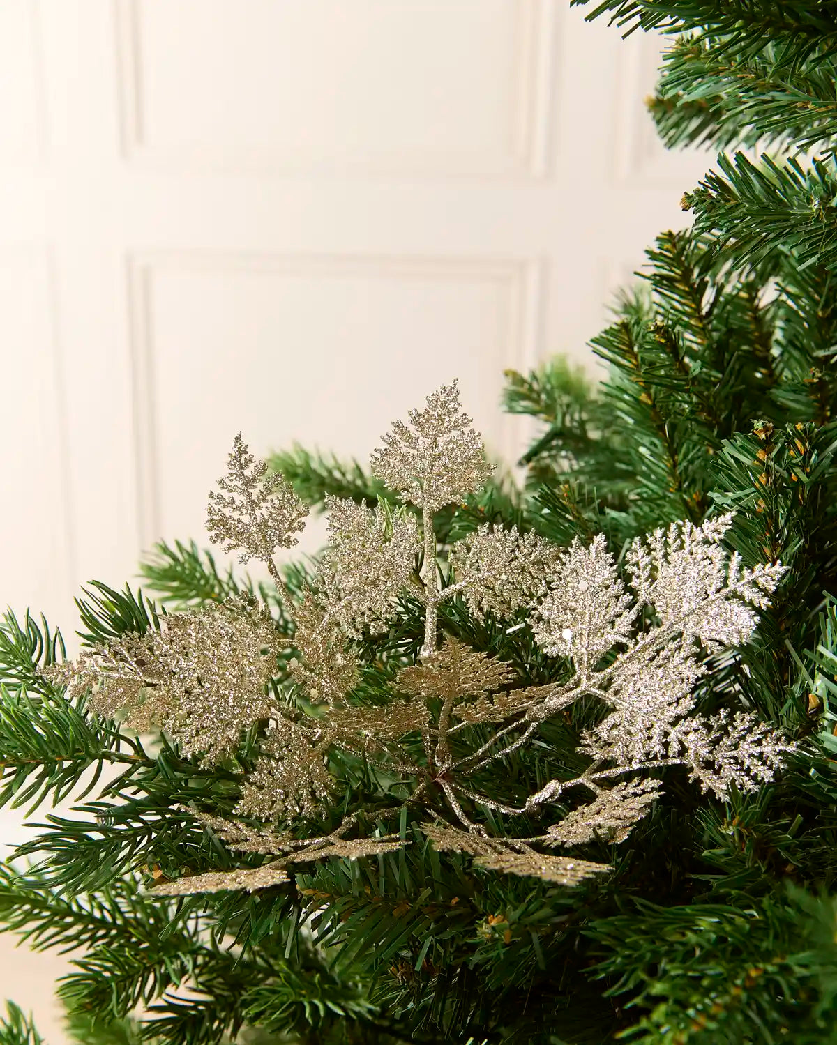 Set of three 19 cm latte glitter leaf picks arranged among green Christmas tree branches.