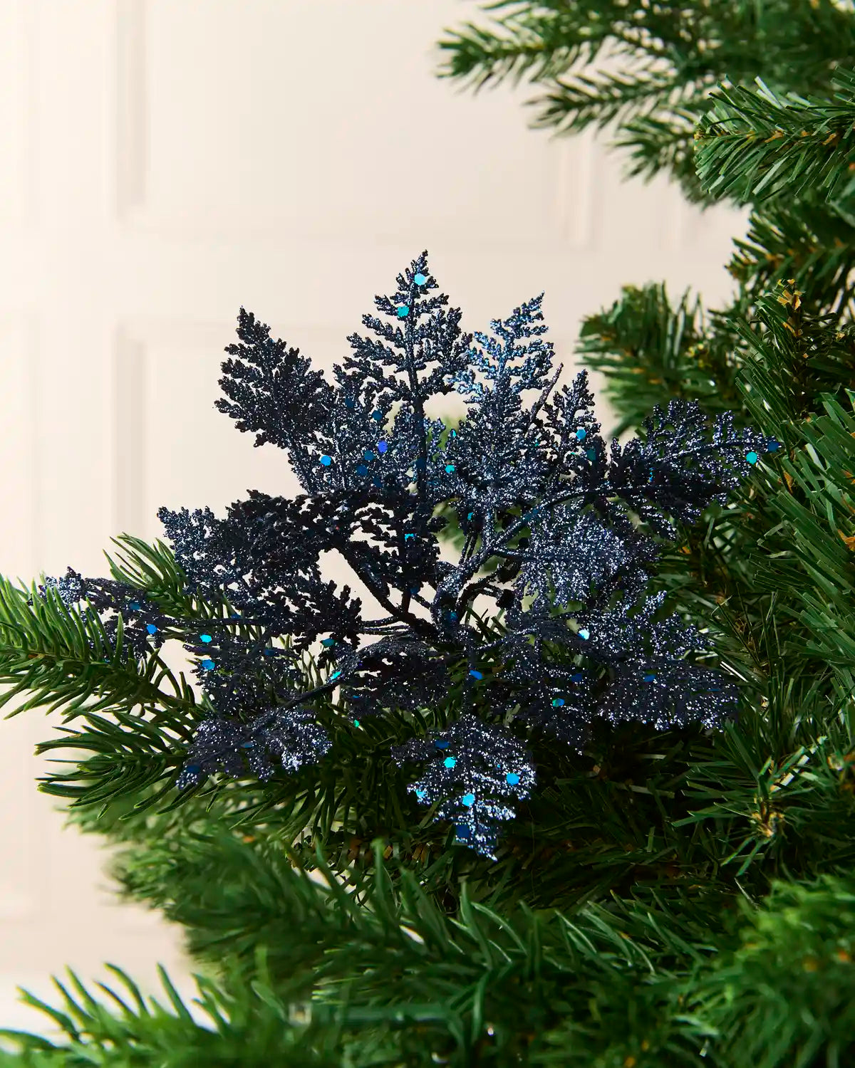 Set of three 19 cm navy glitter leaf picks arranged among green Christmas tree branches.
