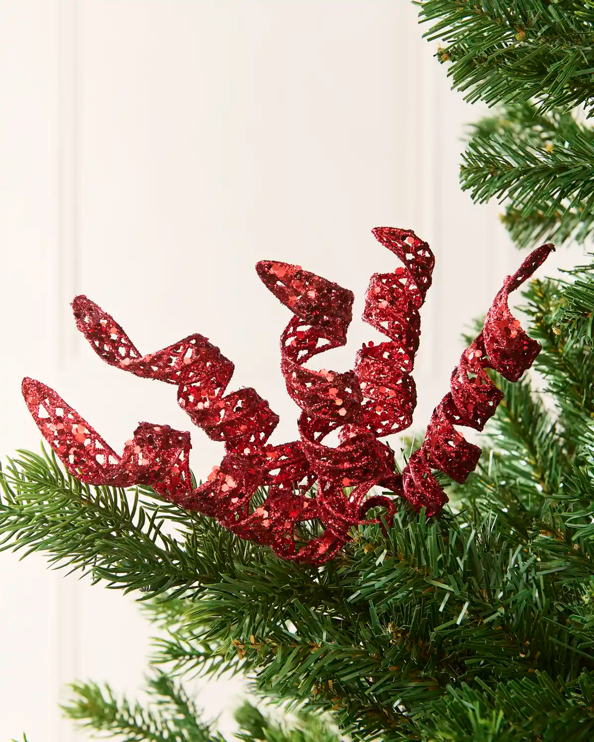 Set of three 18 cm red glitter spiral picks arranged among green Christmas tree branches.