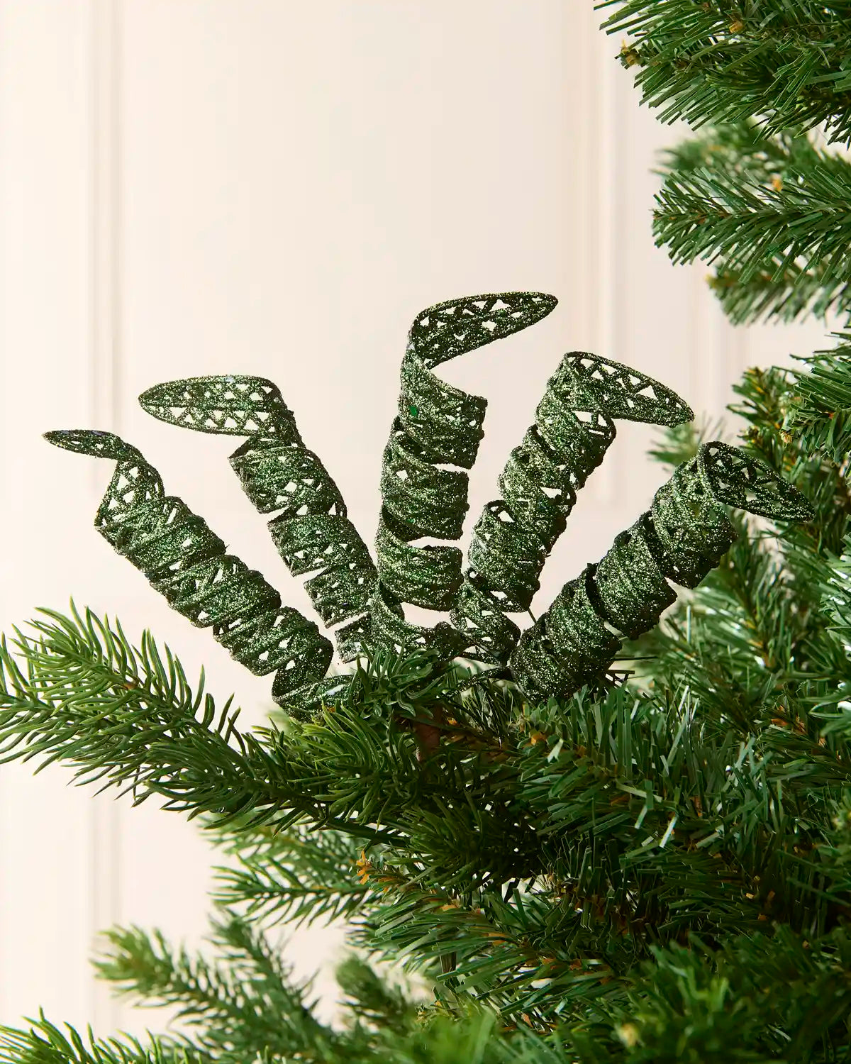 Set of three 18 cm sage green glitter spiral picks arranged among green Christmas tree branches.