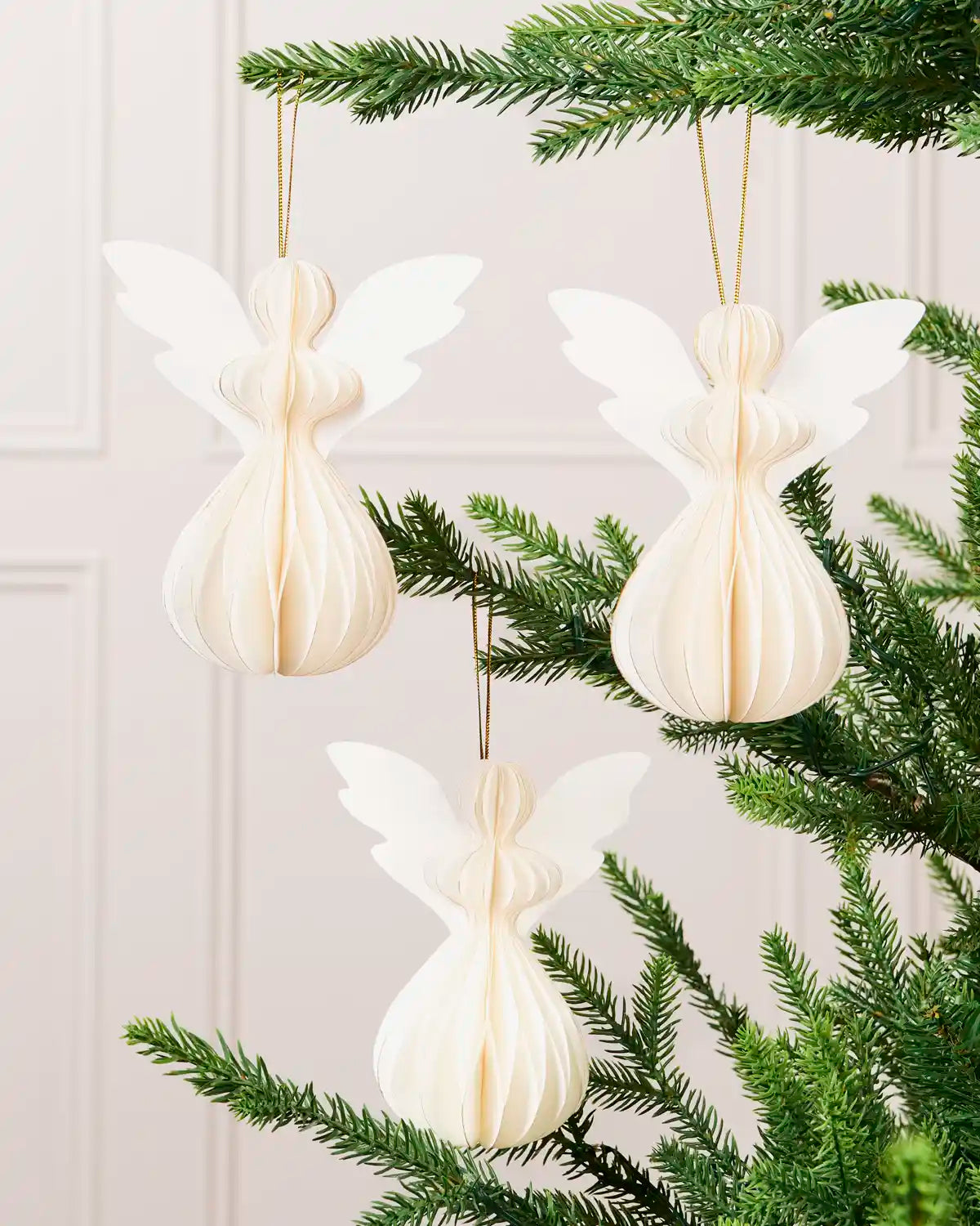 Off-white paper angel decorations from a set of six displayed on a Christmas tree.
