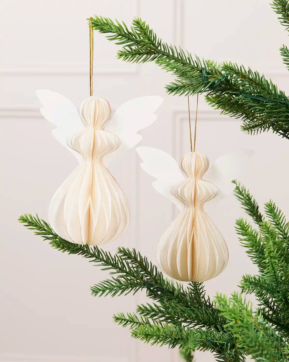 Two off-white 13 cm paper angel decorations hanging from a green Christmas tree.