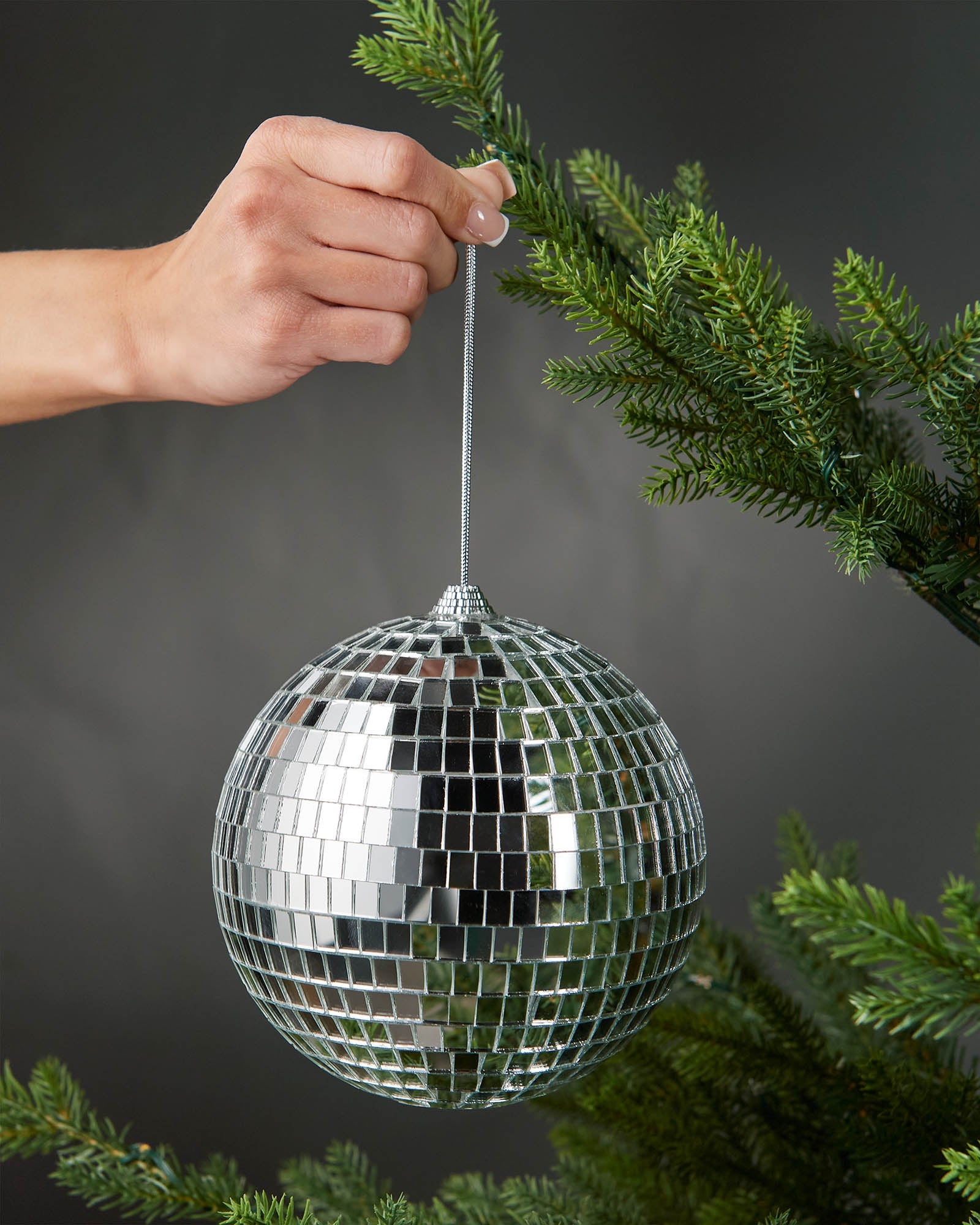 Hand holding a silver 15cm oversized disco ball bauble beside a Christmas tree.