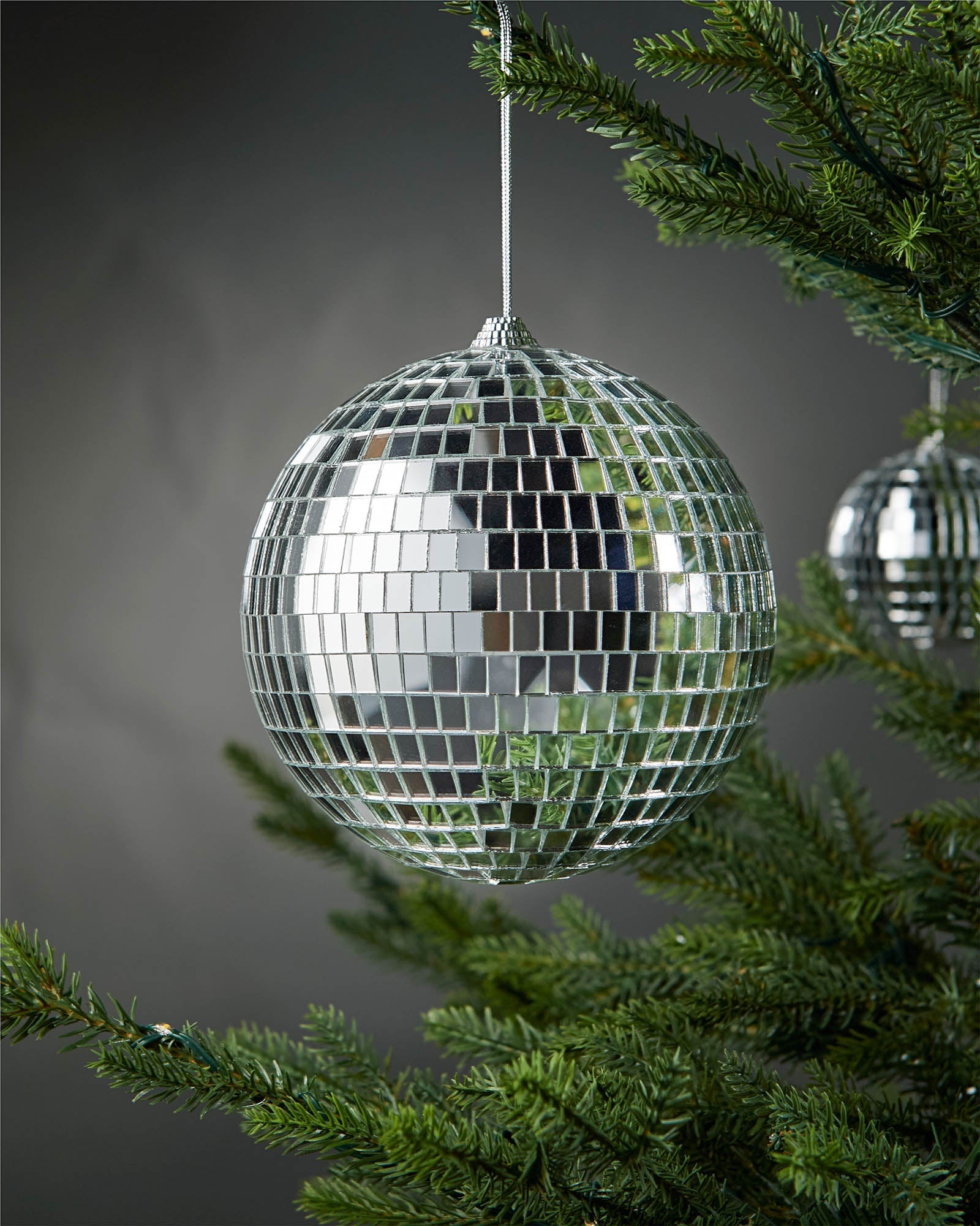 Silver 15cm oversized disco ball bauble hanging on a Christmas tree.