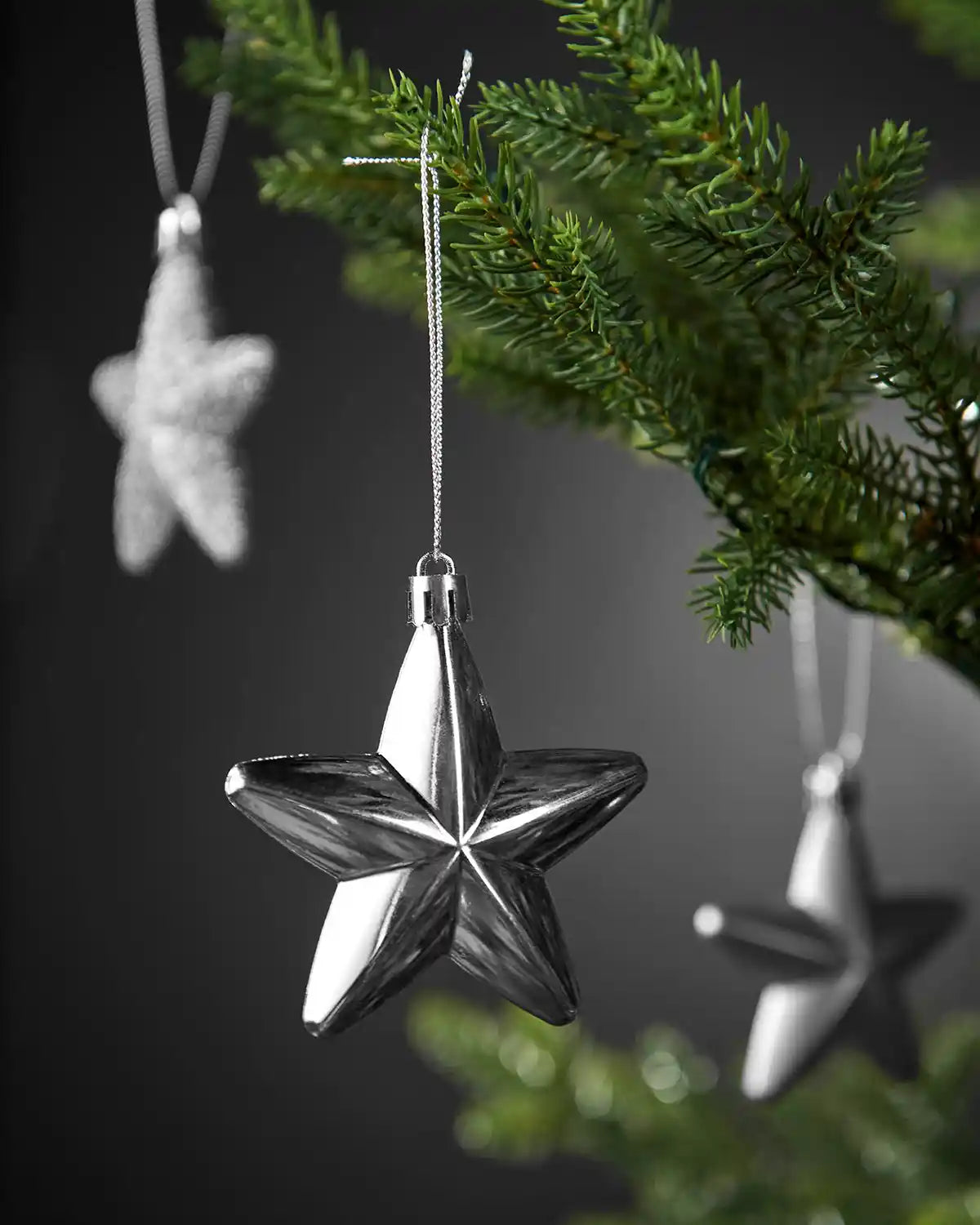 Close-up of a shiny silver 7cm hanging star with silver string on a Christmas tree.