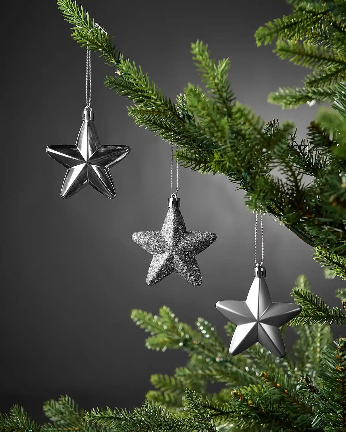 Silver 7cm hanging star decorations in shiny, glitter and matte finishes displayed on a Christmas tree.