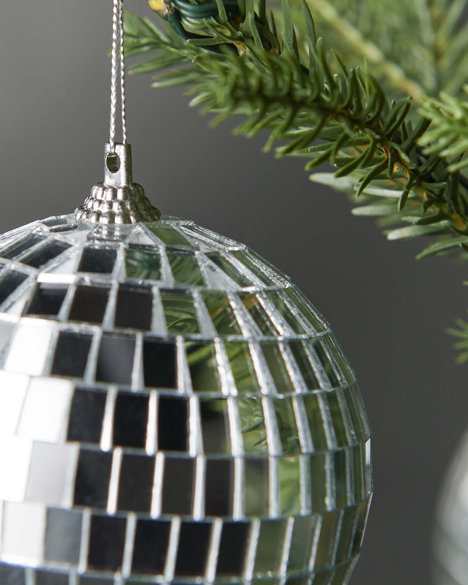 Hand holding a silver 8cm disco ball bauble beside a Christmas tree.