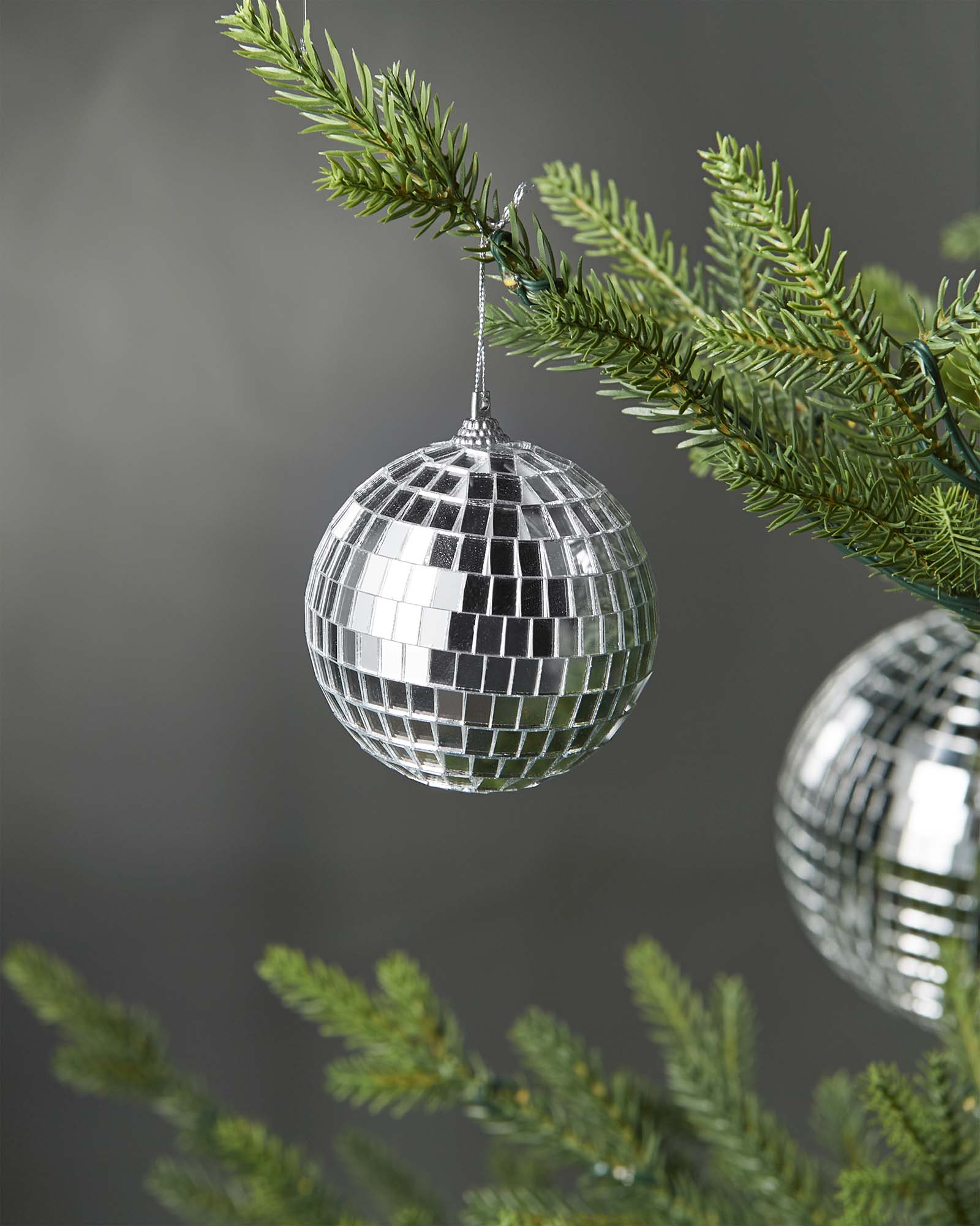 Silver 8cm disco ball bauble hanging on a Christmas tree branch.