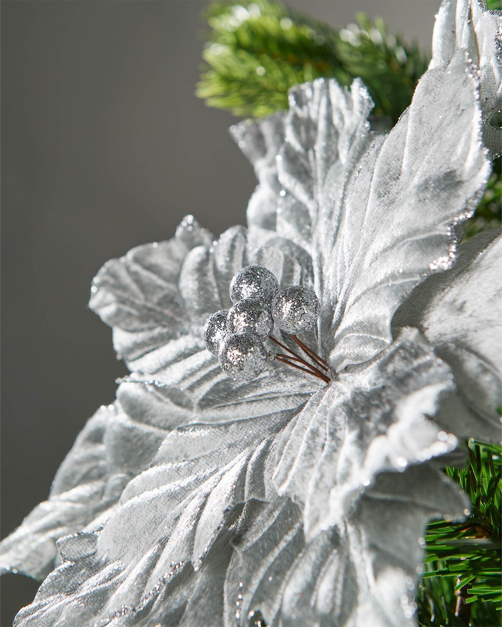 Close-up of a silver artificial poinsettia flower with glittered edges and silver berry centre.