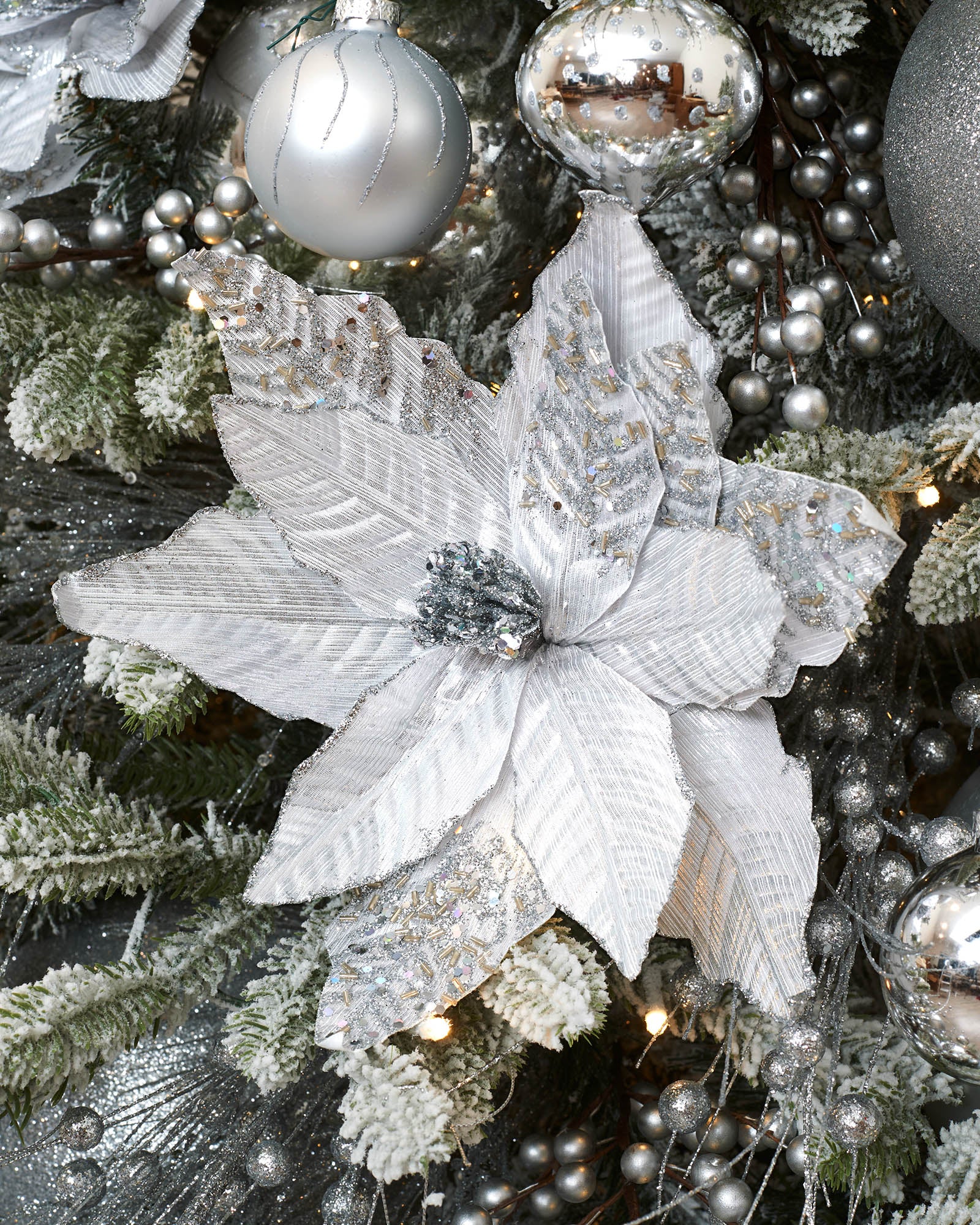 30 cm silver artificial poinsettia flower displayed on a frosted Christmas tree with silver baubles and festive decorations.