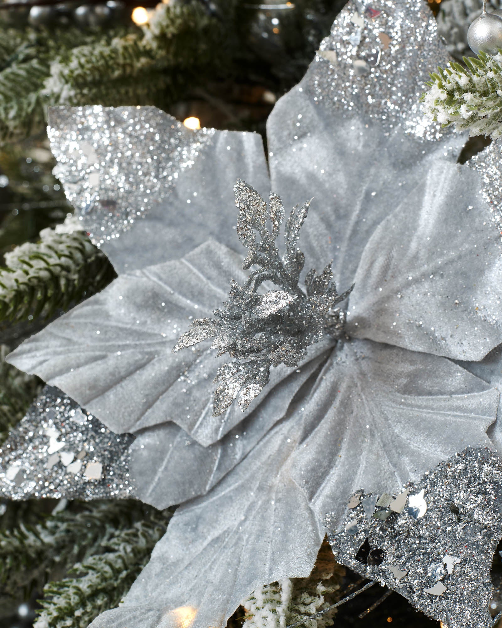 Close-up of a silver artificial poinsettia flower with glitter detailing and textured petals.