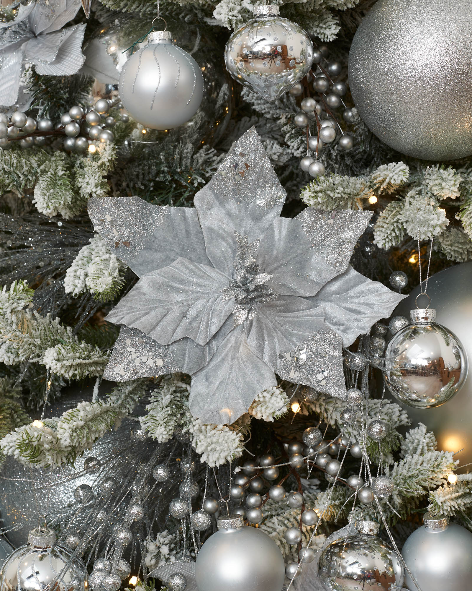 Silver artificial poinsettia flower with glittered petal tips displayed on a decorated Christmas tree.