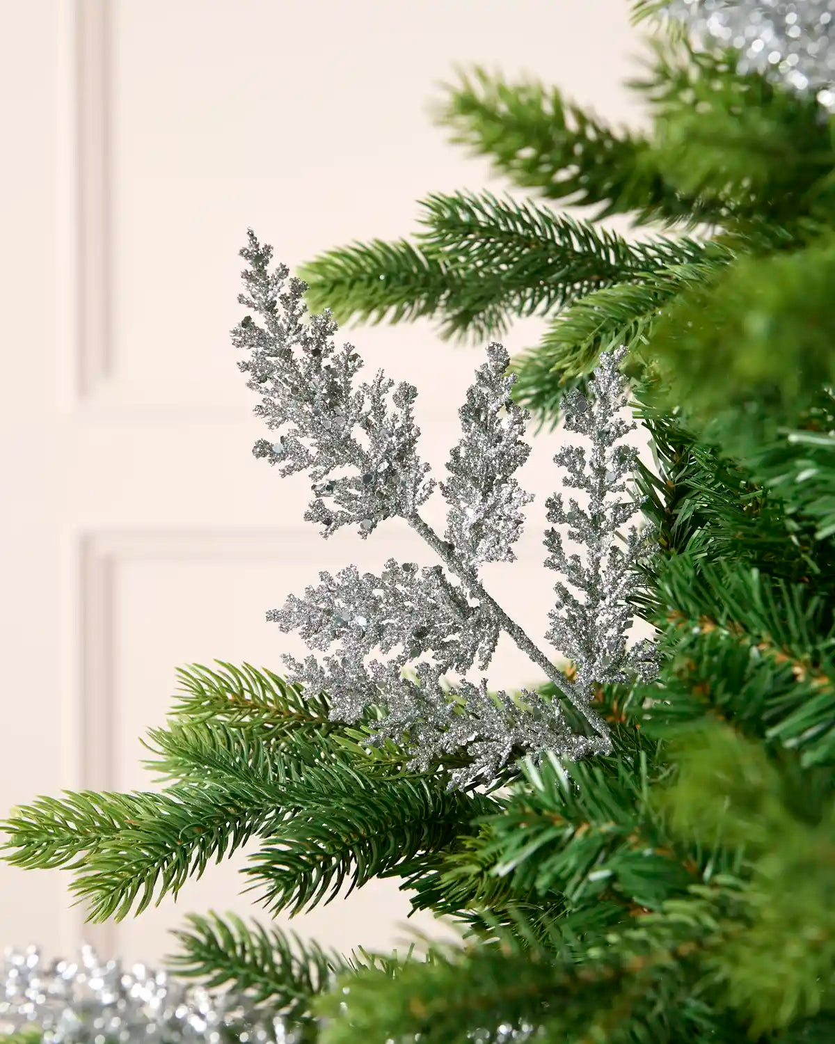 Silver glitter leaf pick arranged amongst green Christmas tree branches.