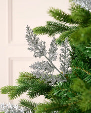 Silver glitter leaf pick arranged amongst green Christmas tree branches.