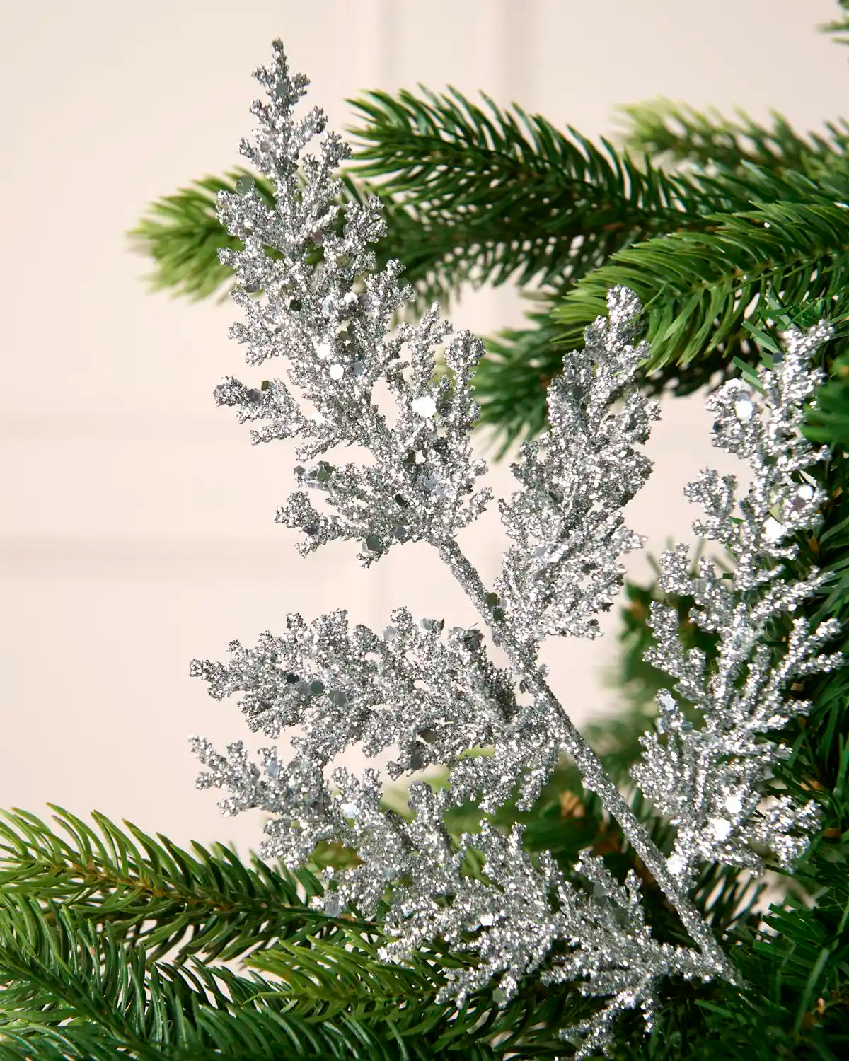 Close-up of a silver glitter leaf pick with reflective sequin detail amongst Christmas tree foliage.
