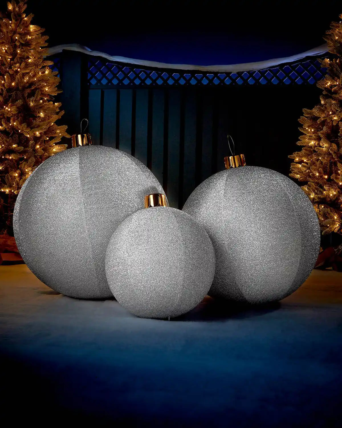 Silver inflatable tinsel Christmas baubles in different sizes displayed outdoors with warm festive lights.