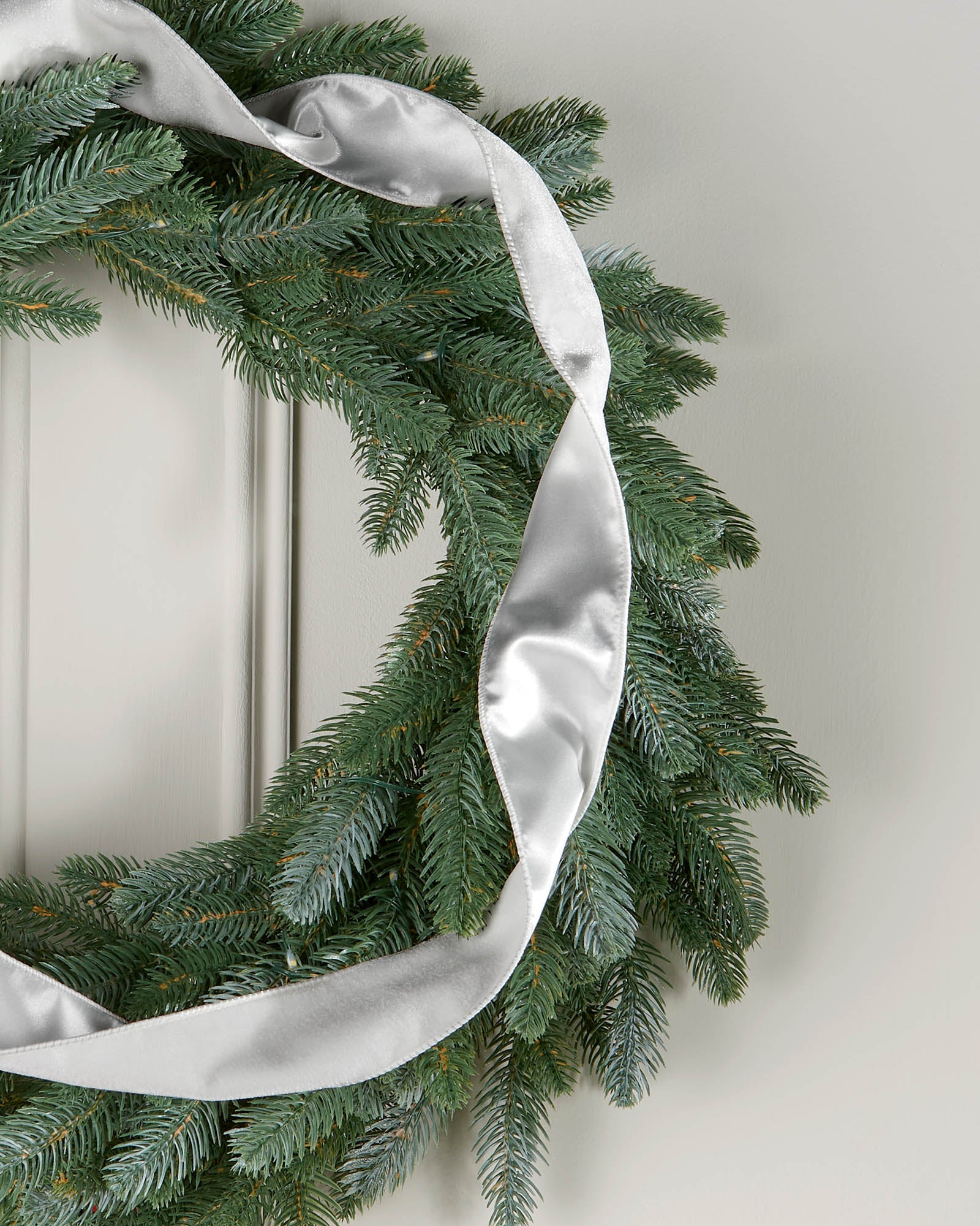 Silver velvet ribbon styled in a loose spiral on a green Christmas wreath.