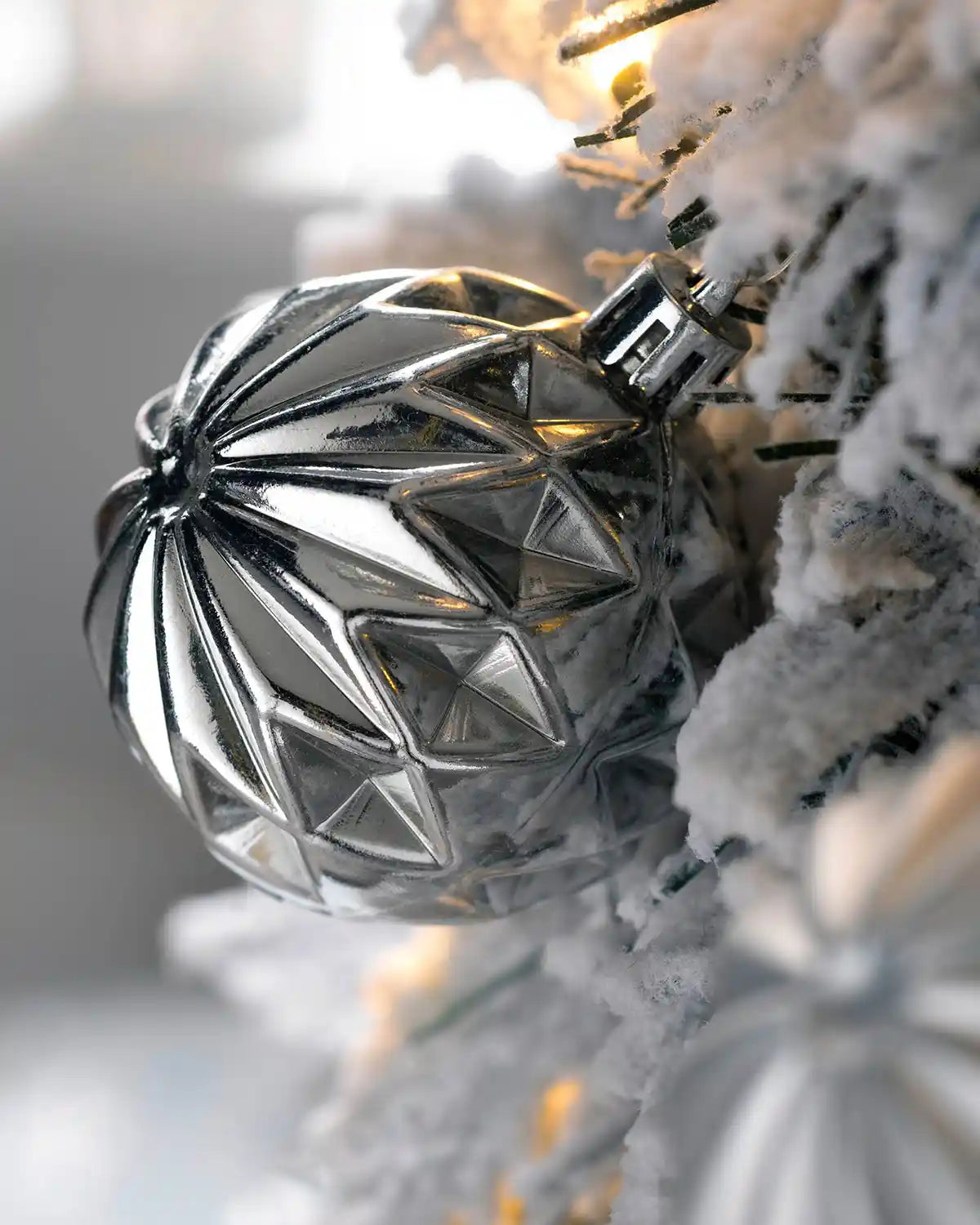 Close-up of a silver bauble and warm white lights on snowy branches