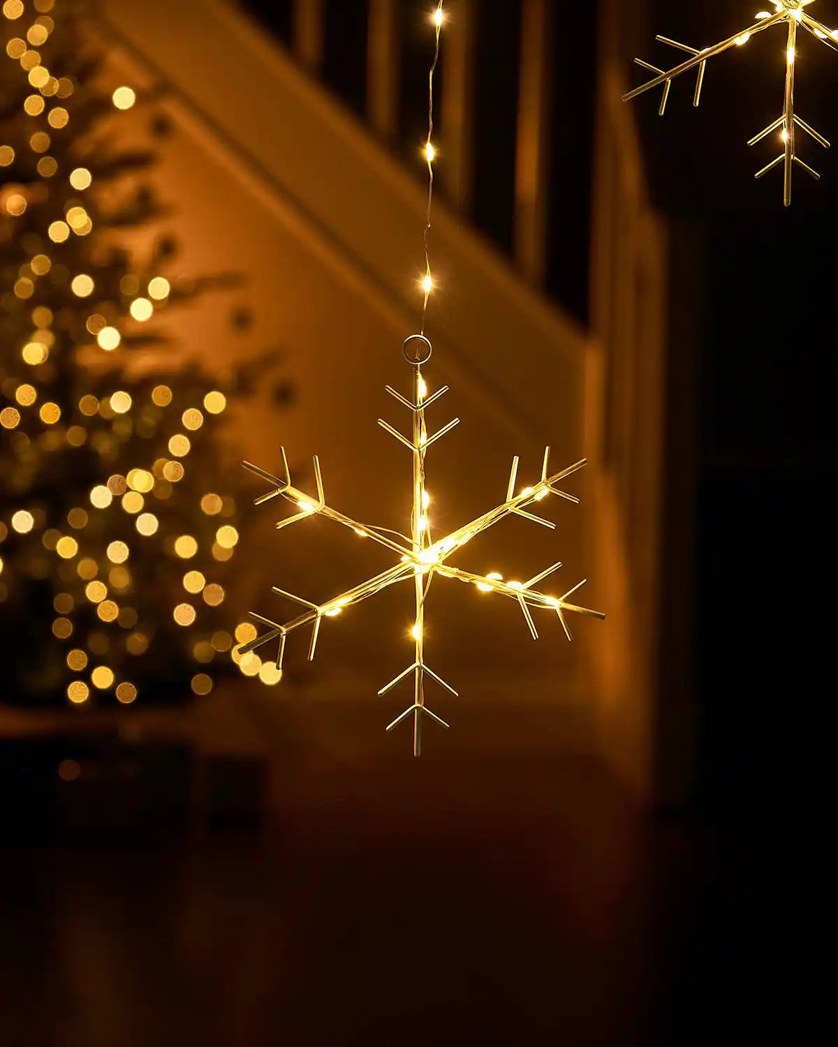 Illuminated warm white LED snowflake hanging from curtain string lights