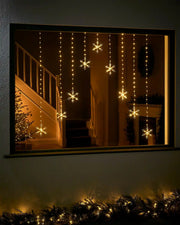 Warm white snowflake curtain string lights displayed in a festive window at night