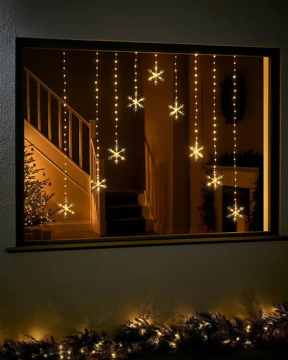 Warm white snowflake curtain string lights displayed in a festive window at night