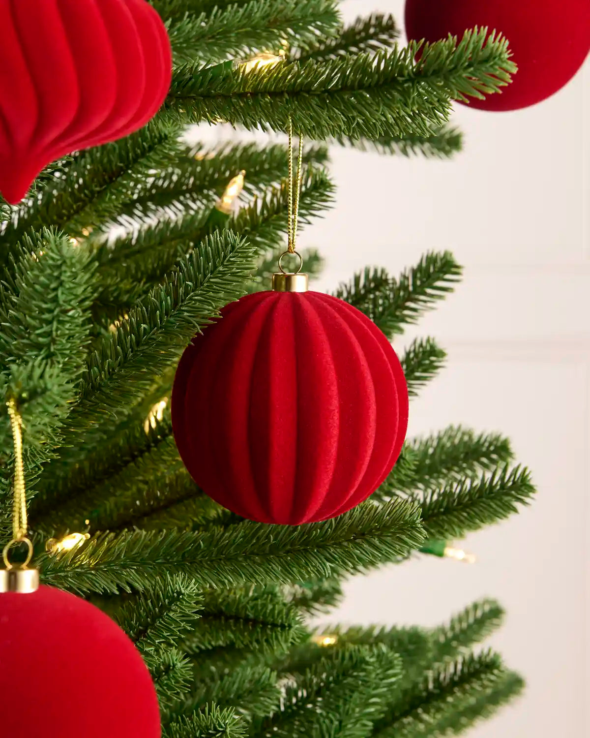 spiral and ribbed velvet baubles hanging on a Christmas tree with gold string against a light background