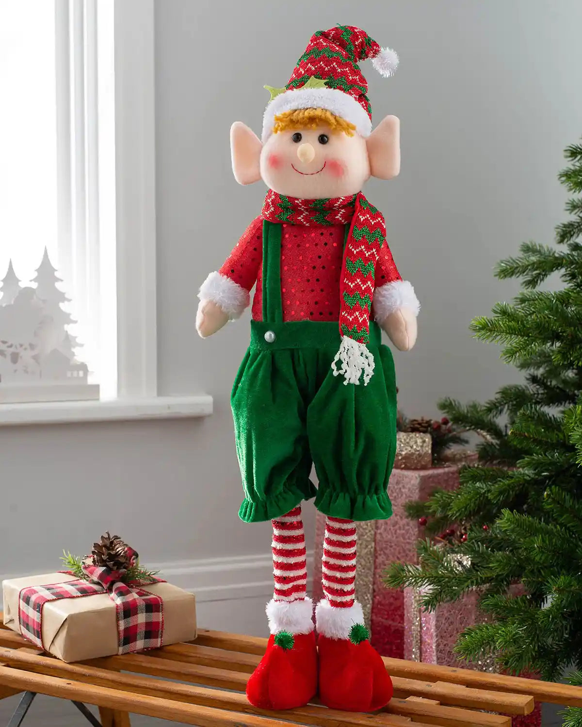 Standing elf boy figurine, 60 cm, displayed on a bench beside Christmas presents and a tree