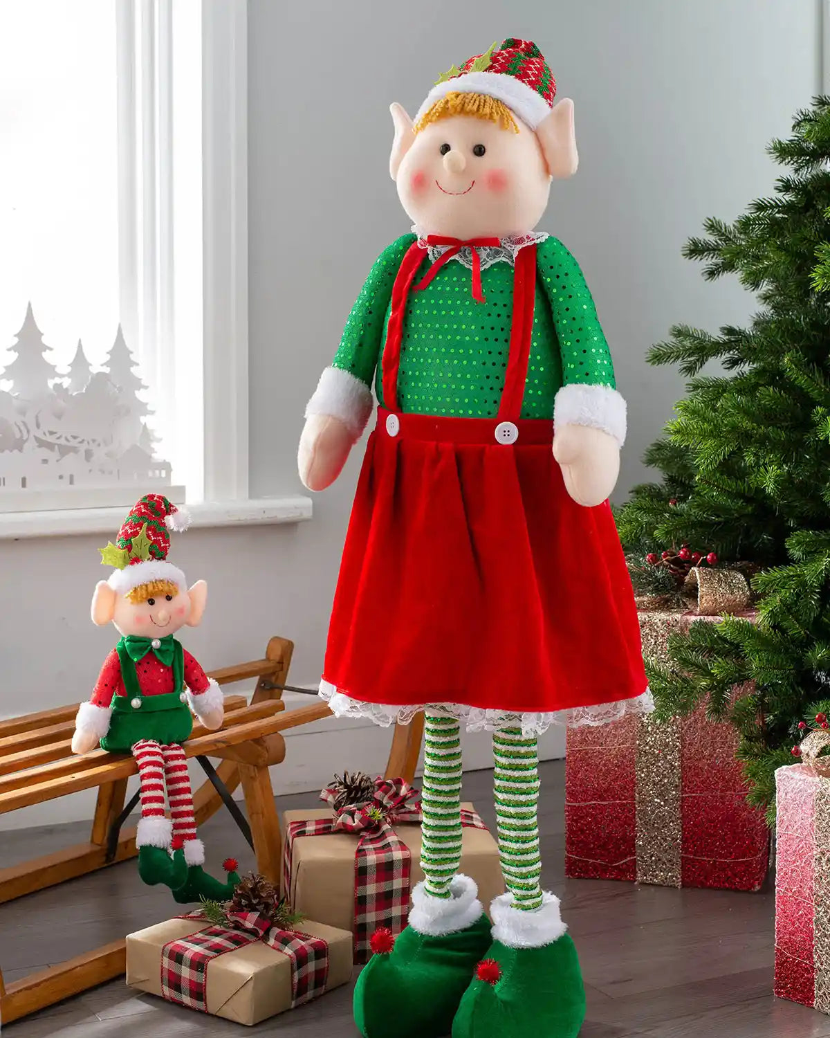 Standing elf girl figurine with extendable legs displayed beside Christmas presents and a tree