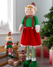 Standing elf girl figurine with extendable legs displayed beside Christmas presents and a tree