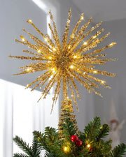 Gold starburst Christmas tree topper lit with warm white LEDs on top of a Christmas tree