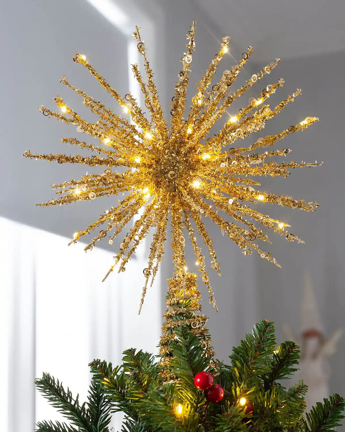 Gold starburst Christmas tree topper lit with warm white LEDs on top of a Christmas tree
