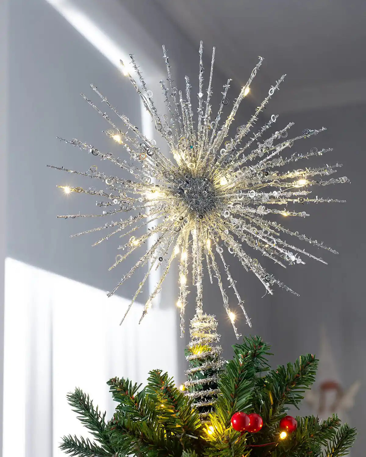 Silver starburst Christmas tree topper lit with warm white LEDs on top of a Christmas tree