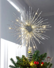 Silver starburst Christmas tree topper lit with warm white LEDs on top of a Christmas tree