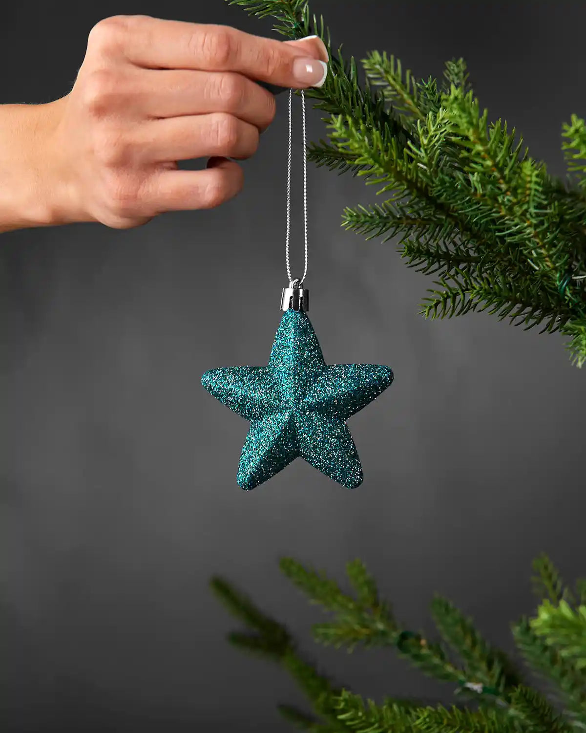 Teal glitter star decoration being hung on a Christmas tree branch with a silver string.