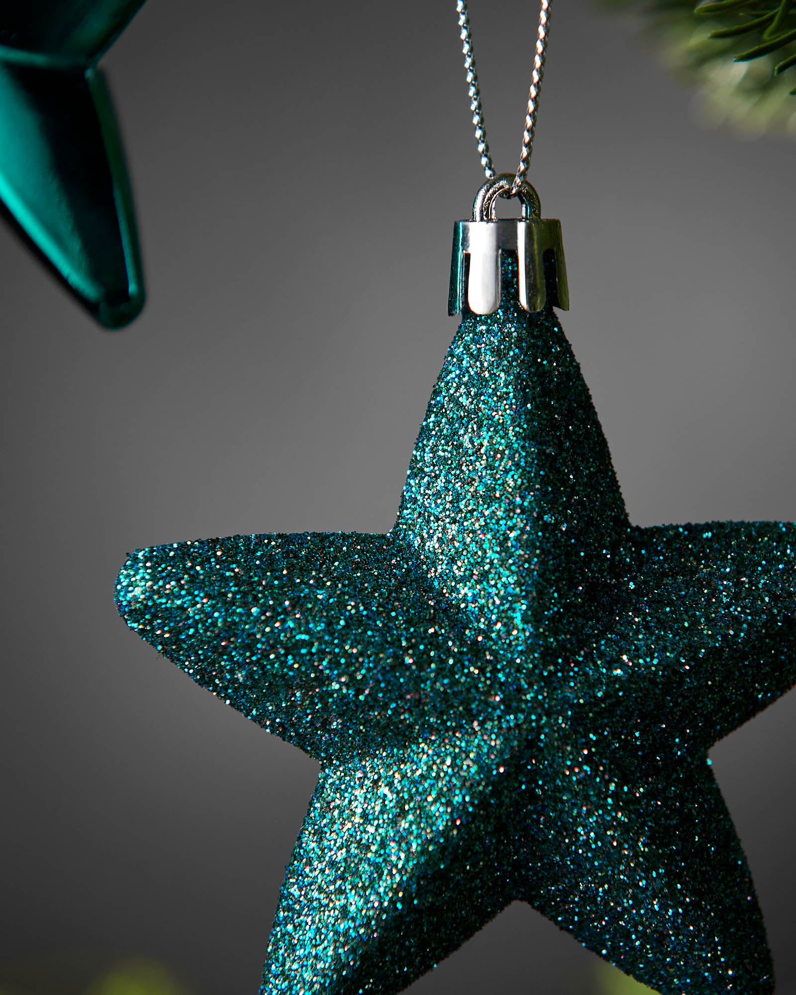 Detail close-up of a teal glitter 7cm star decoration with a silver hanging string.