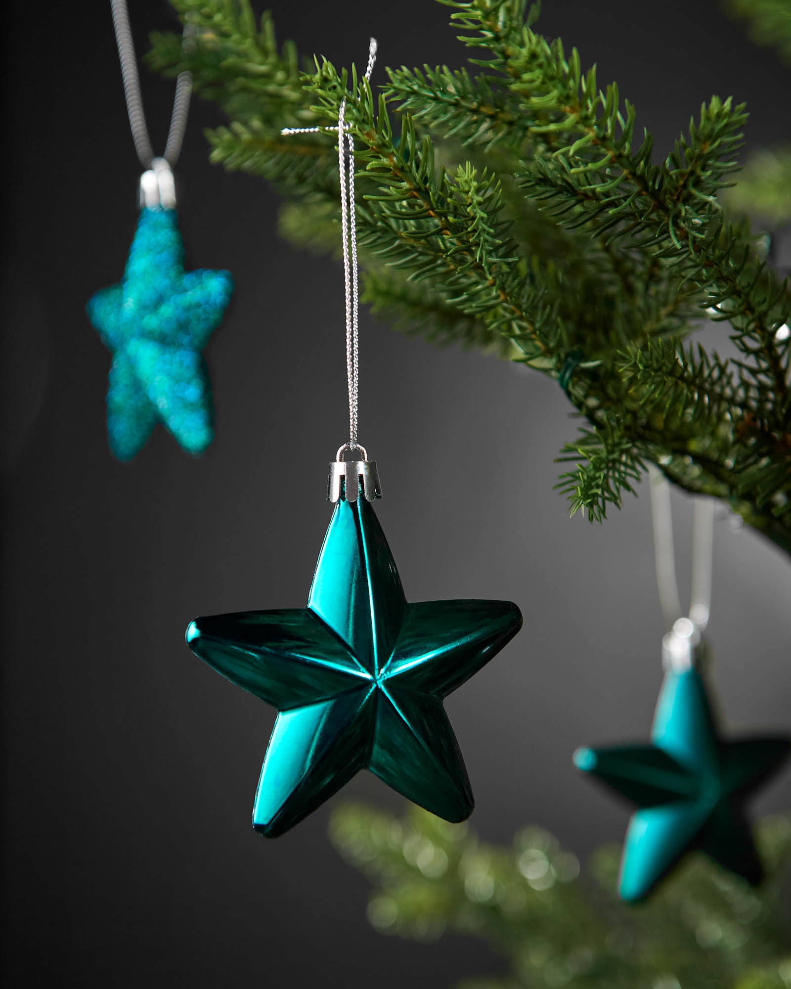 Close-up of a shiny teal star Christmas decoration hanging from a tree branch.